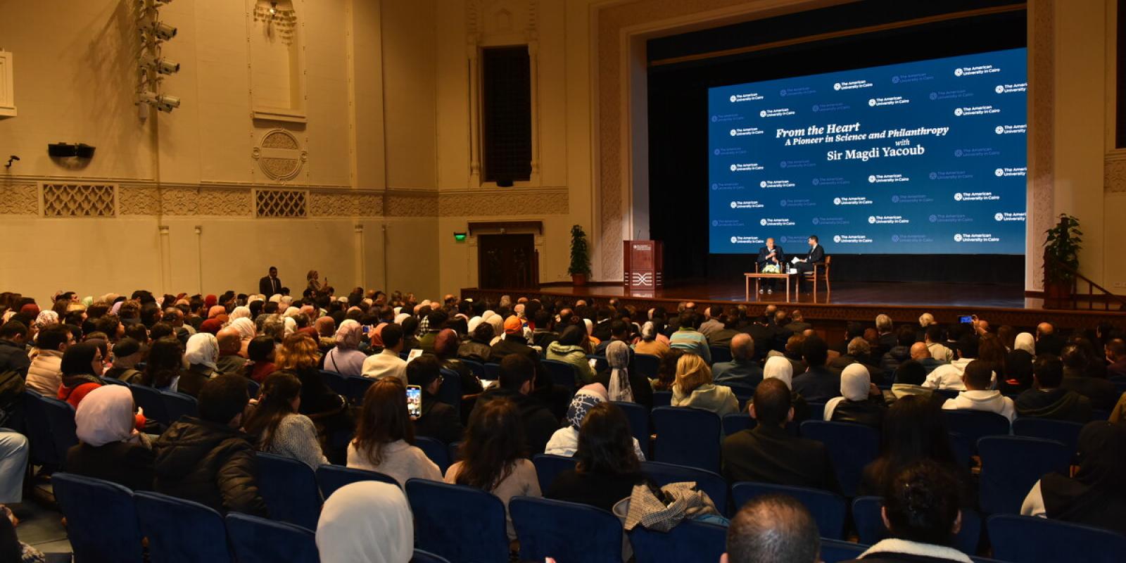 People sitting in a hall listening to people on stage