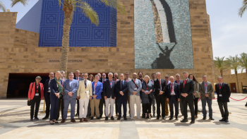 Many people in business casual wear pose in front of a tall beige building