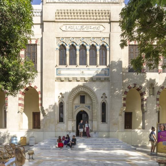 Female and male students walking on campus in front large Islamic building with three flags on the top
